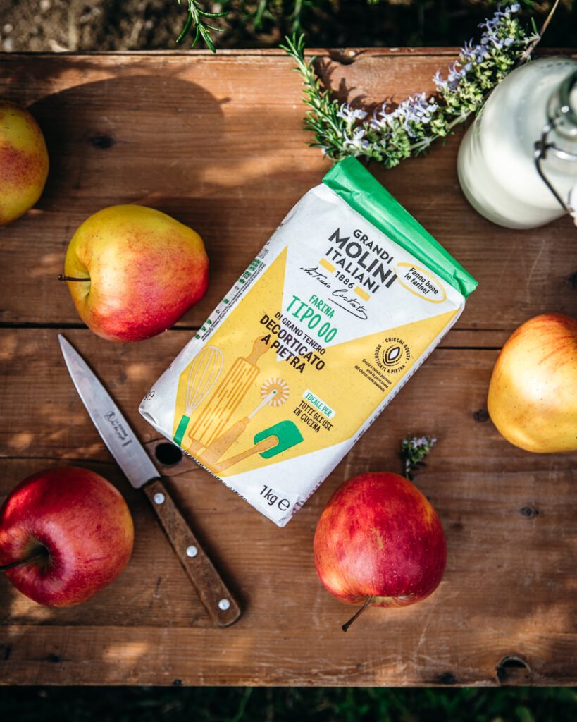 farina Grandi Molini Italiani tipo 00 decorticata a pietra con mele fresche su tavolo in legno
